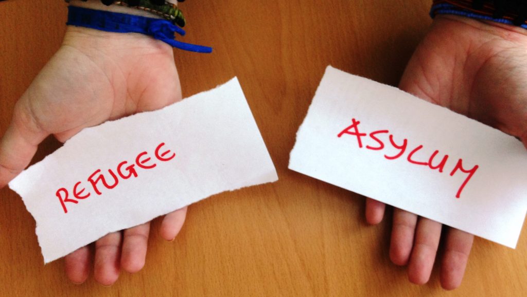 hands showing the words refugee and asylum